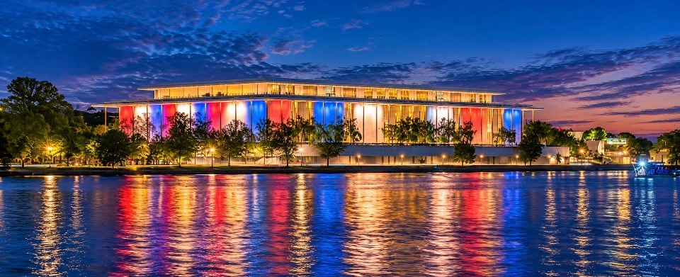 Kennedy Center for the Performing Arts illuminated at dusk with red and blue reflections on the Potomac River