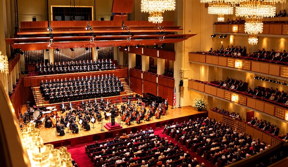 Kennedy Center Concert Hall interior with full orchestra choir and audience under crystal chandeliers