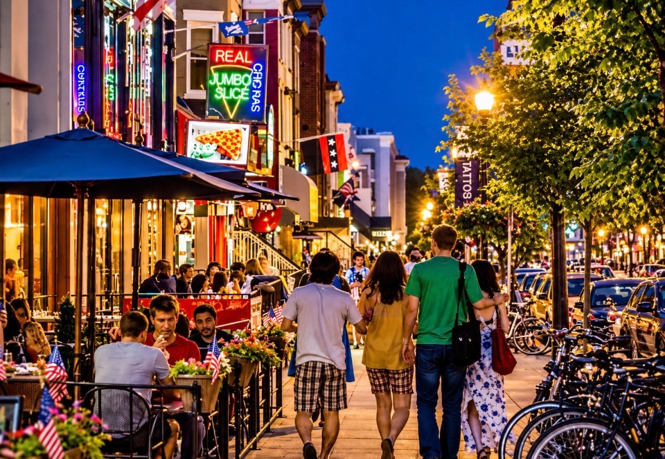 Adams Morgan DC street scene at dusk with neon signs restaurants and pedestrians