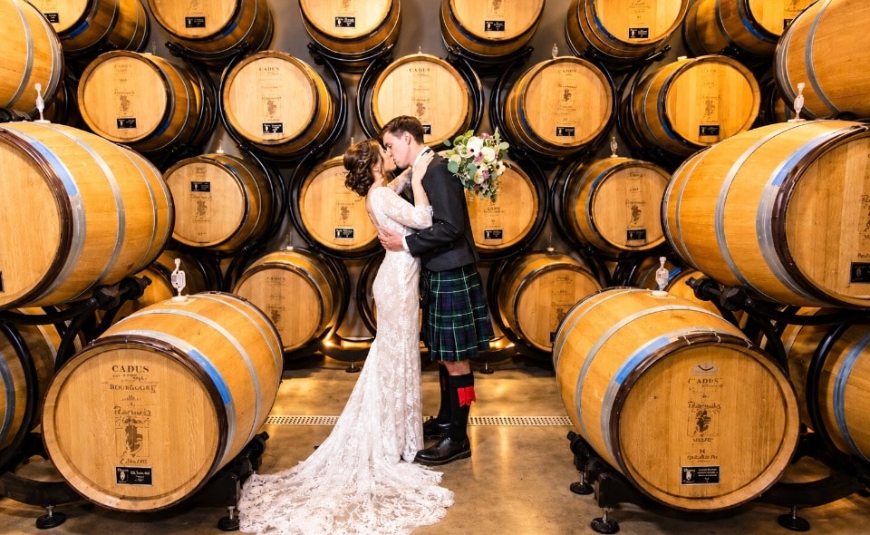 Wedding couple kissing in front of wine barrel wall at Pearmund Cellars winery