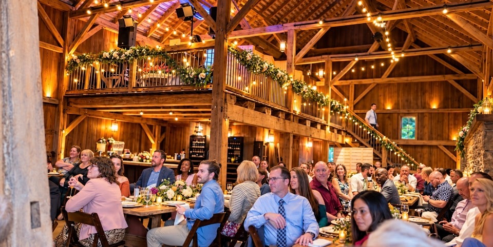Elegant barn winery event with guests dining under string lights and loft balcony